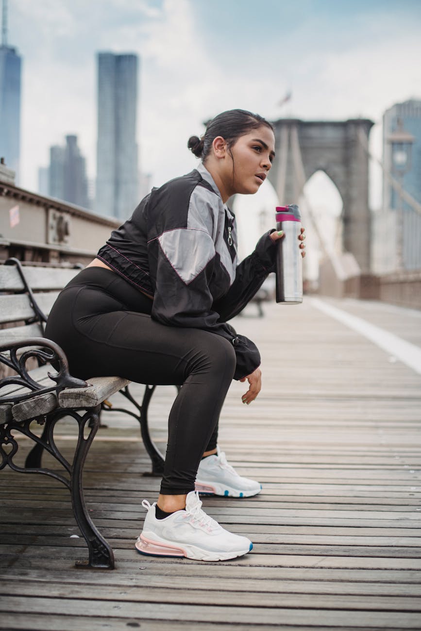 woman in sports clothing sitting on a bench and drinking water